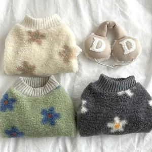 Flat lay of plush knitted pet sweaters with floral patterns and lettered earmuffs on white fabric