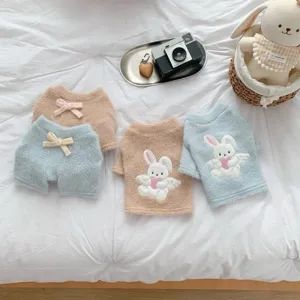 Flat lay showing fuzzy pastel pet garments with rabbit appliqués and bow details on white bedding