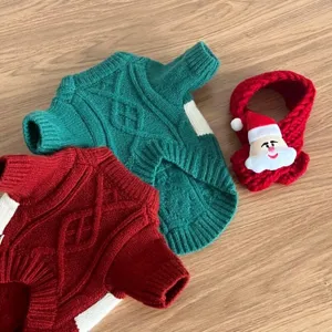 Deux pulls torsadés pour animaux, vert et rouge, près d’une écharpe rouge brodée d’un père Noël