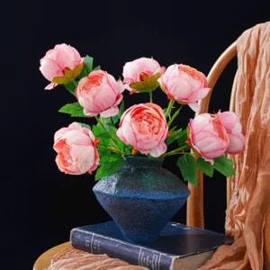 Peonías rosas en un jarrón azul oscuro texturizado, sobre libros ante un fondo oscuro