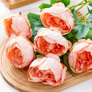 Primer plano de pétalos de tela rosa melocotón y hojas verdes dispuestos sobre una bandeja de madera