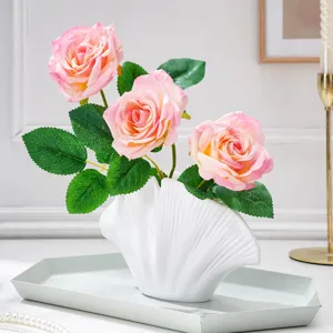 Trois roses dégradées avec feuilles vertes dans un vase blanc mat en céramique, forme coquillage