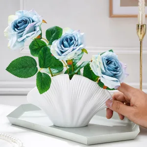 Gros plan sur des roses bleu dégradé et leurs feuilles vertes dans un vase coquillage blanc nervuré