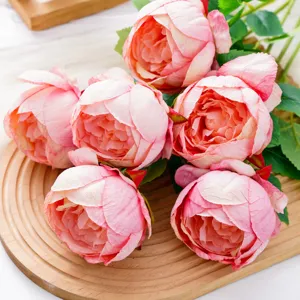 Primer plano de peonías artificiales rosas con pétalos en capas sobre una bandeja redonda de madera