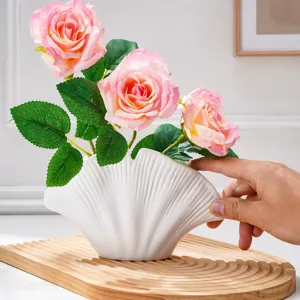 Vase en céramique blanche nervurée, en forme de coquillage, avec des roses roses sur un plateau en bois