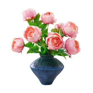 Ramo artificial de peonías rosas con hojas verdes en un jarrón de cerámica azul oscuro