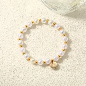 Perlenarmband mit goldenen Zwischenperlen und A-Anhänger, von oben auf cremefarbenem Grund