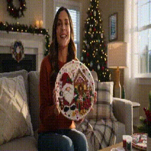 Een vrouw toont een ovale kerstschotel met kerstmanmotief in een feestelijk versierde woonkamer