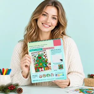 Une femme tient un livre de coloriage spiralé aux scènes de Noël colorées, sur fond vert menthe
