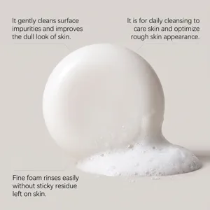 Close-up of a smooth white round cleansing bar with airy foam on a soft light gray background