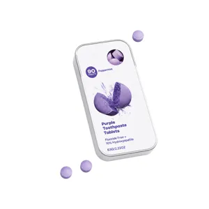 Purple peppermint toothpaste tablets in a metal tin, with loose tablets on a white background