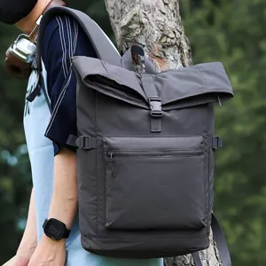 Zaino grigio scuro con chiusura arrotolata, tasca frontale con zip e fibbia, indossato all’aperto