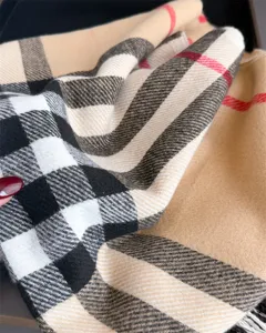 Gros plan sur une écharpe à carreaux pliée, beige, noire et blanche, avec de fines lignes rouges