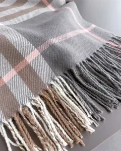 Gros plan sur le tissu à carreaux gris, aux lignes roses et beiges, avec des franges assorties.