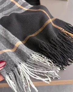 Gros plan sur un foulard doux à carreaux noirs et gris, rayures orange et bordures à franges