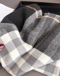 Gros plan sur une écharpe douce à carreaux noirs, gris et crème, au tissage fin, dans une boîte