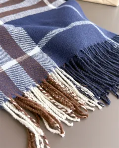 Gros plan sur le tissu à carreaux bleu marine, crème et brun, avec des franges tissées au bord