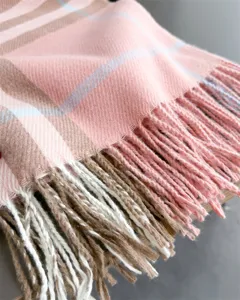 Gros plan sur le tissu doux d’une écharpe à carreaux rose, avec des rayures beiges et des franges visibles