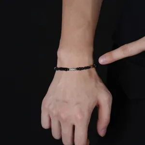 Dettaglio del polso con bracciale di perline nere, una perla argentata incisa e accenti marroni