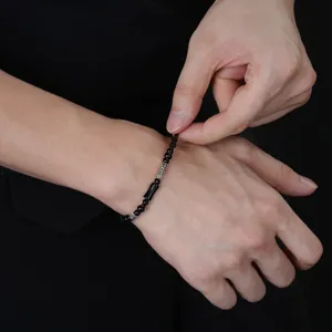 Primo piano di un bracciale con perline nere e dettagli argentati mentre viene allacciato al polso