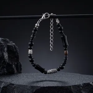 Bracciale di perline nere con dettagli argentati, moschettone e catena di prolunga su pietra scura