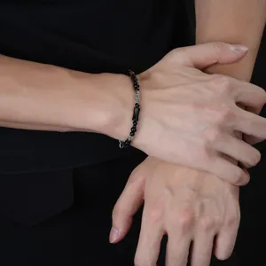 Dettaglio di bracciale nero con perline a forma di bambù e inserti argentati indossato al polso