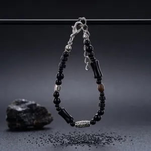 Bracciale nero con perline tonde e tubolari, catena e chiusura color argento, mostrato appeso