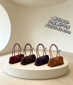 Four suede handbags in burgundy, brown, purple and tan, lined up on a round white display plinth