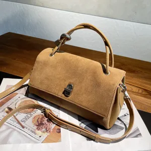 Angled view of a tan suede-textured flap, metal clasp, top handle and adjustable shoulder strap
