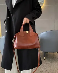 A person holds a brown leather bag with gold-tone hardware and a long detachable shoulder strap