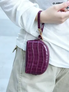 Close-up of a plum croc-embossed half-moon pouch with wrist strap and gold-tone zipper