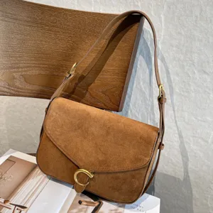 Dettaglio della texture scamosciata marrone, della chiusura dorata e della tracolla regolabile della borsa