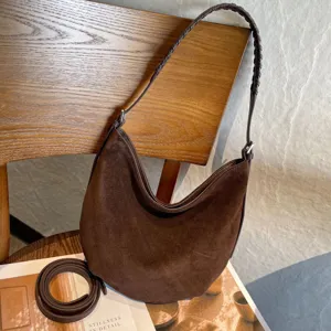 Sac demi-lune en suède marron, poignée tressée et bandoulière amovible sur table en bois