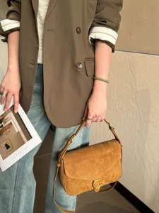 Borsa a tracolla in camoscio marrone, patta curva e fibbia dorata, con look casual
