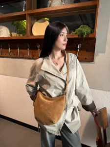 Une femme porte un sac souple en daim brun en forme de demi-lune avec un trench clair