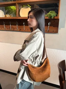 Vue de profil d’un modèle portant un sac brun effet daim, forme croissant et fine bandoulière