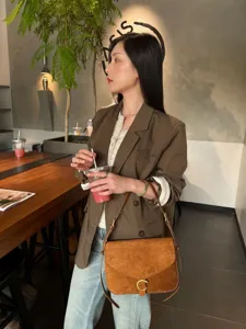 Borsa a tracolla in camoscio marrone con chiusura dorata a C, indossata con un blazer al caffè