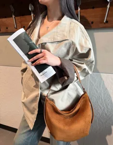 Vue en situation d’un sac demi-lune brun effet daim, porté à l’épaule avec une bandoulière tressée