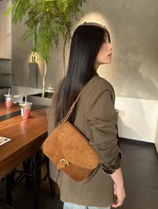 Vista laterale di una donna con borsa marrone in camoscio e fibbia ad anello dorata in un caffè