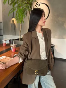 Una donna indossa una borsa marrone effetto suede con fermaglio dorato in un café luminoso