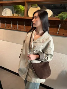 Modèle portant un sac demi-lune brun en suédine, à fine bandoulière, sur une veste beige