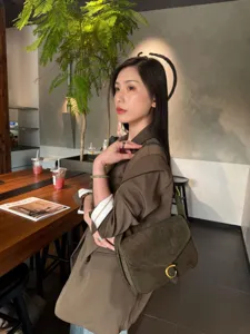 Donna con borsa a tracolla in suede verde oliva, con patta e chiusura ad anello dorata, in un caffè