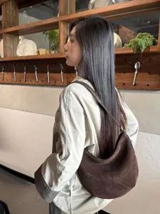 Vue de profil d’un modèle portant un sac demi-lune brun effet suédé avec bandoulière tressée