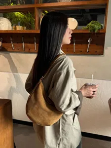 Vue lifestyle d’un modèle portant un sac brun en daim, en demi-lune, avec une anse tressée