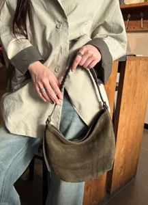 Une personne tient un sac en suédine vert olive, à la silhouette arrondie et à l’anse tressée