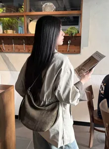 Profil d’une femme portant un sac demi-lune en suédine brun olive dans un café lumineux