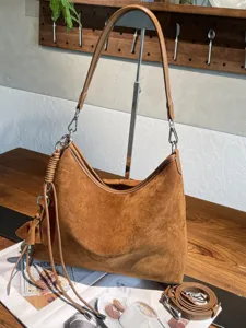 Braune Veloursledertasche auf Holztisch mit abnehmbarem Riemen und geflochtenem Quastenanhänger