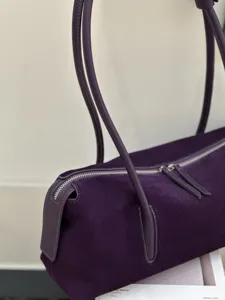 Close-up view of a purple suede bag with matching leather handles and a silver zipper