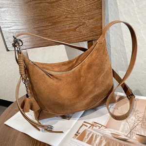 Brown suede-textured bag on a tabletop, with a zip opening, leather strap and silver hardware.