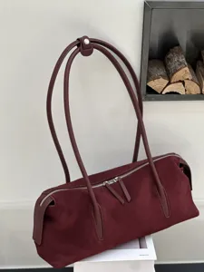 Detail of a burgundy suede-textured bag with leather trim, twin handles and silver zipper